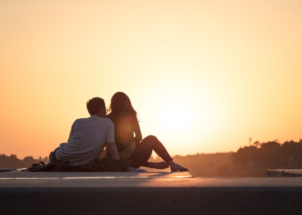 a couple sitting on rooftop looking at sunset